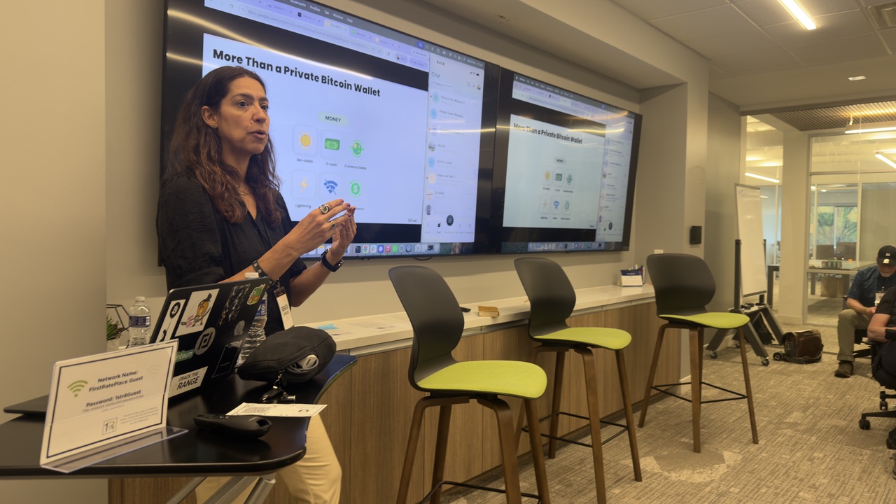 A speaker presents the Fedi community app to summit attendees, with slides showing 'More Than a Private Bitcoin Wallet' on screen